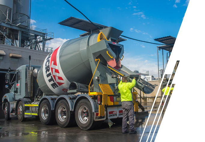 A man in a yellow jacket and gray pants pulls the auger down from a gray cement mixer.