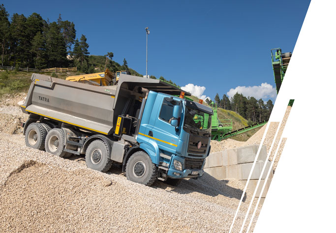 A dump truck travels through dirt piles and towards a sunset.