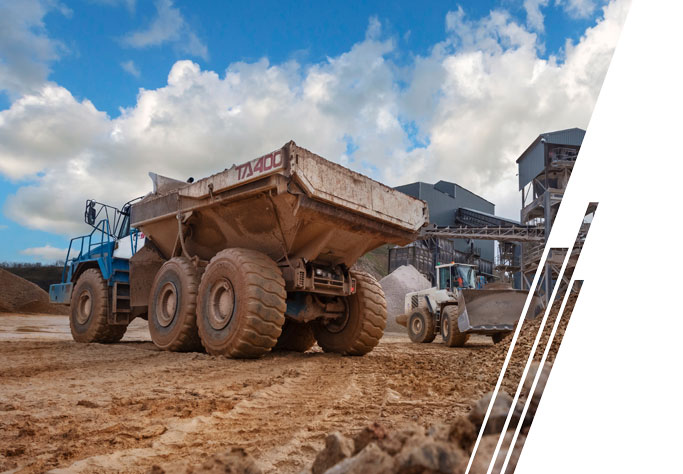 A blue truck with a white mining dump body backs up to an aggregate facility.